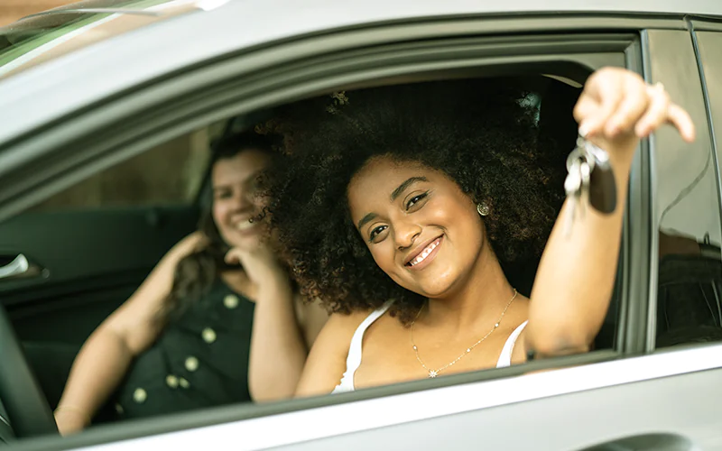 Carro por Assinatura: Duas mulheres dentro do carro. A motorista mostra a chave pela janela.