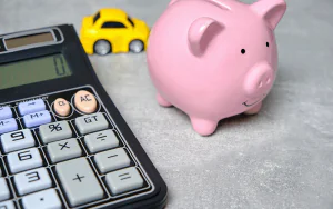 Imagem mostra uma calculadora, um cofre de porquinho e um carrinho de brinquedo.