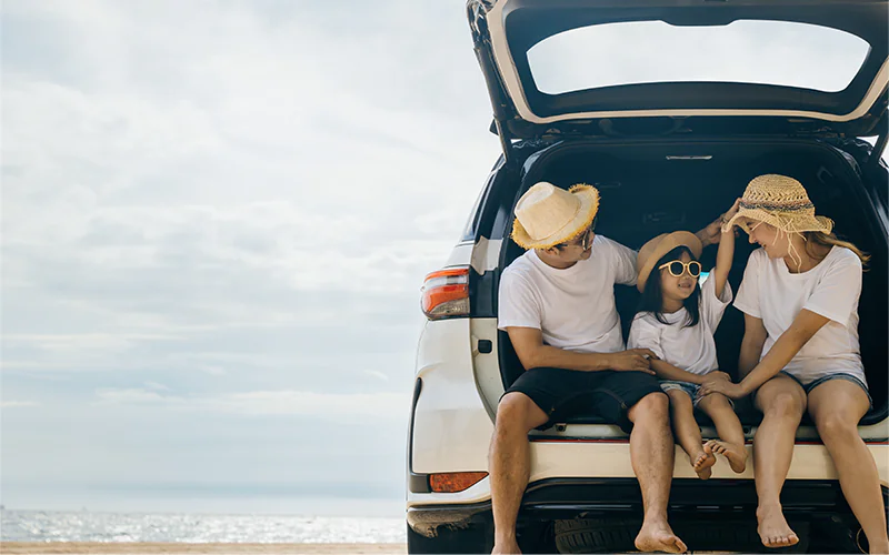 Imagem mostra uma família sentada no porta-malas de um carro estacionado