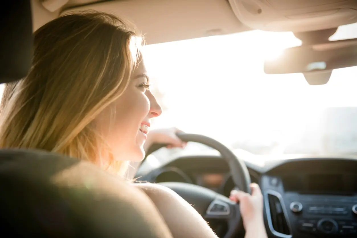mulher sorrindo dirigindo um carro com o dia ensolarado