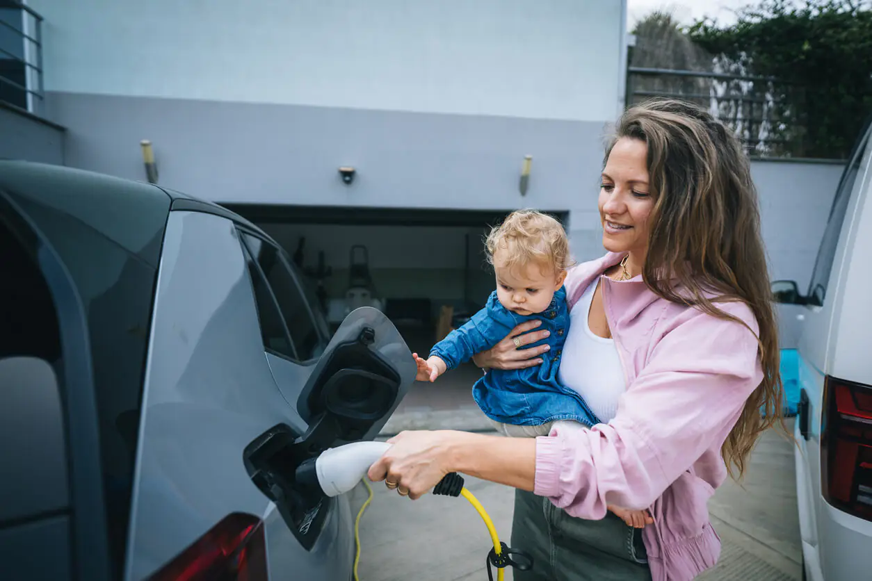 mulher segurando bebê carregando seu carro elétrico em casa