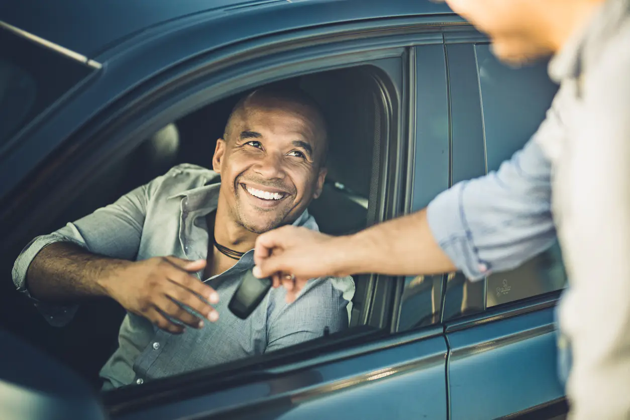 Homem recebendo a devolução da chave de um carro por assinatura.