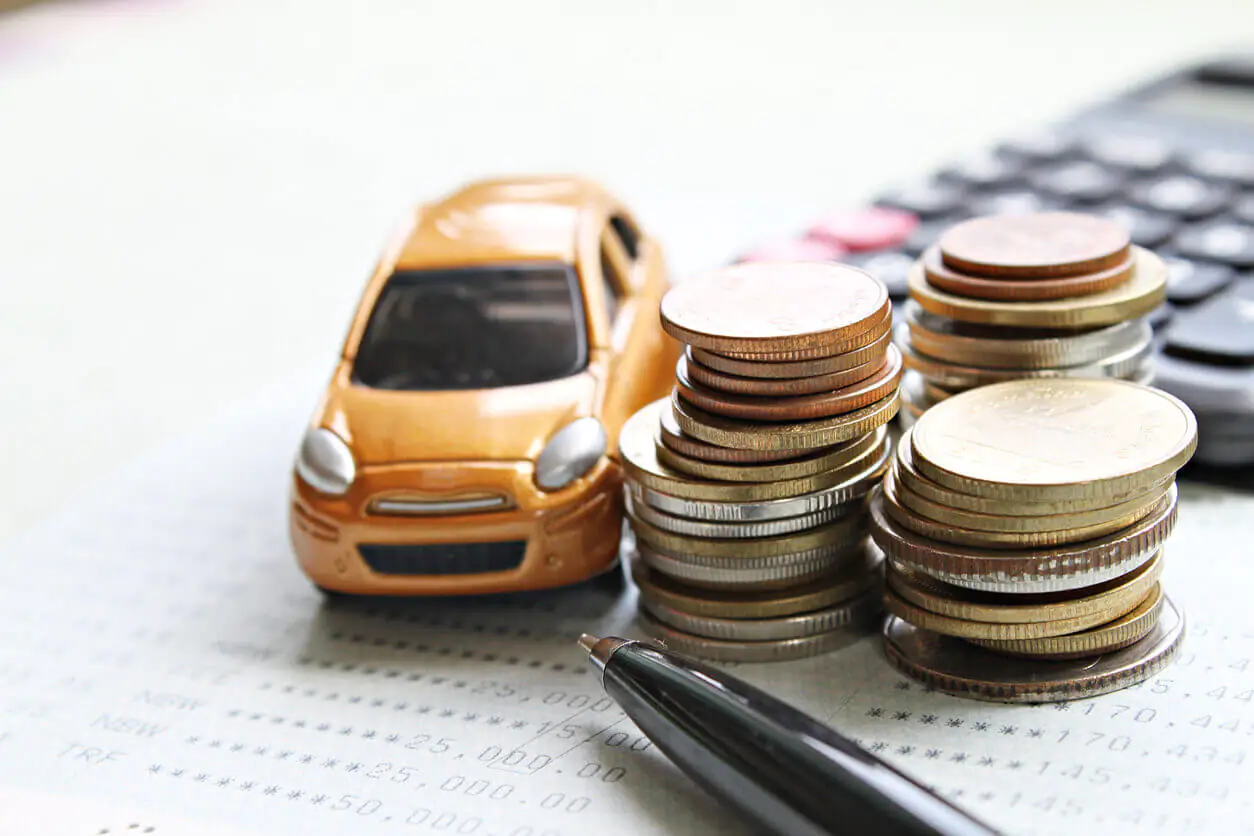 Carro em miniatura, moedas e calculadora sobre a mesa 